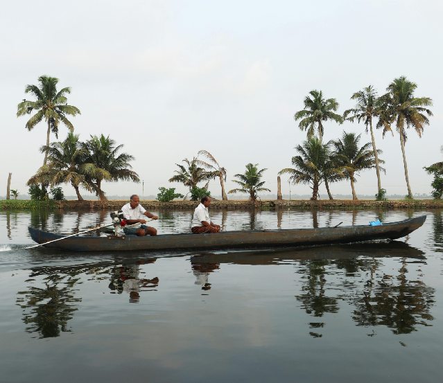 A serene landscape of Kerala's backwaters, with traditional houseboats gliding through lush greenery, symbolizing the tranquil beauty of the region. This image is perfect for Kerala tour packages, highlighting the best time to visit Kerala. It also offers a glimpse into the state's rich history and culture, and provides insights on how to reach Kerala for a memorable experience.